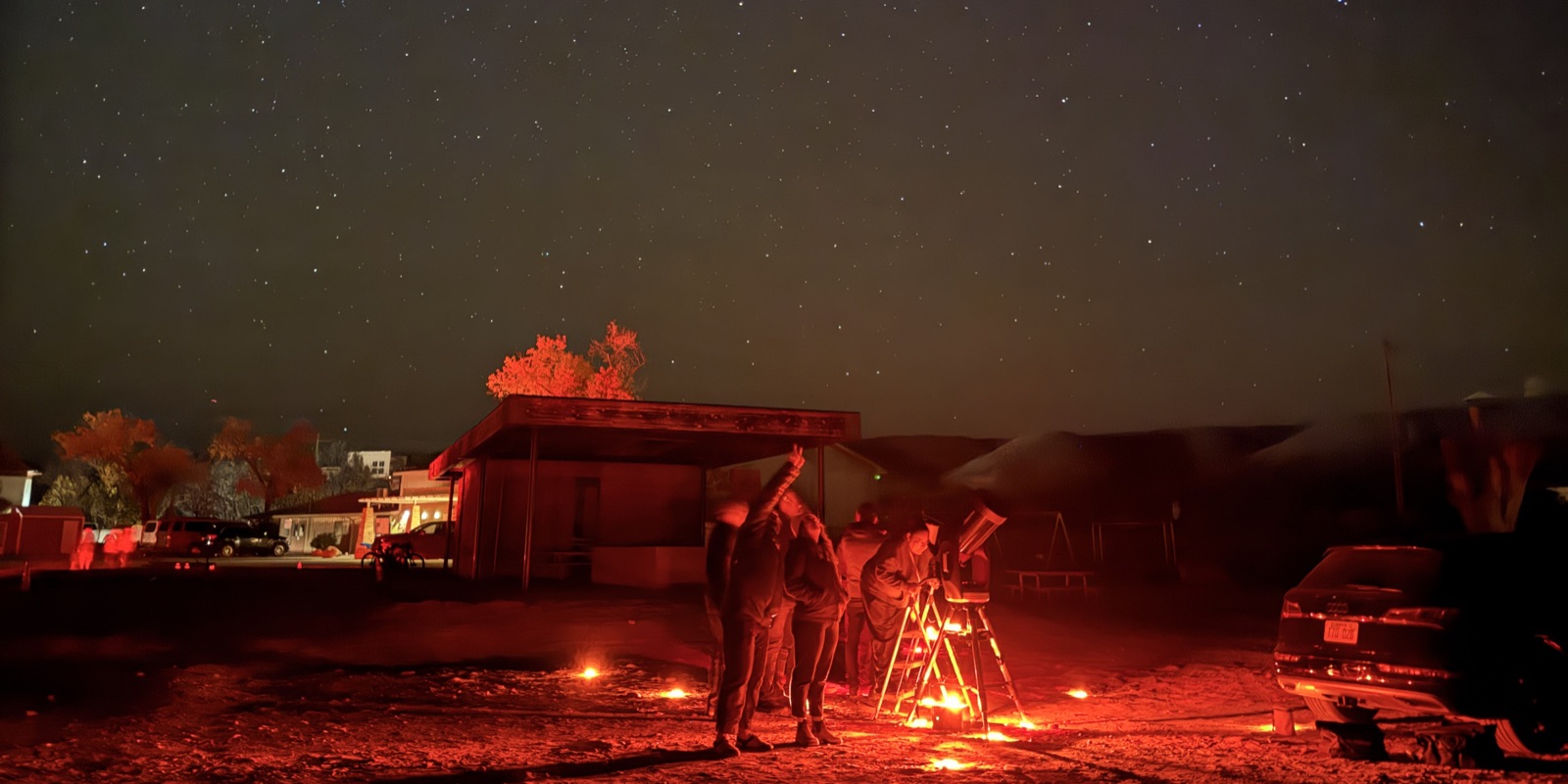 A crowd of visitors gathered around a telescope beside a tour van at night