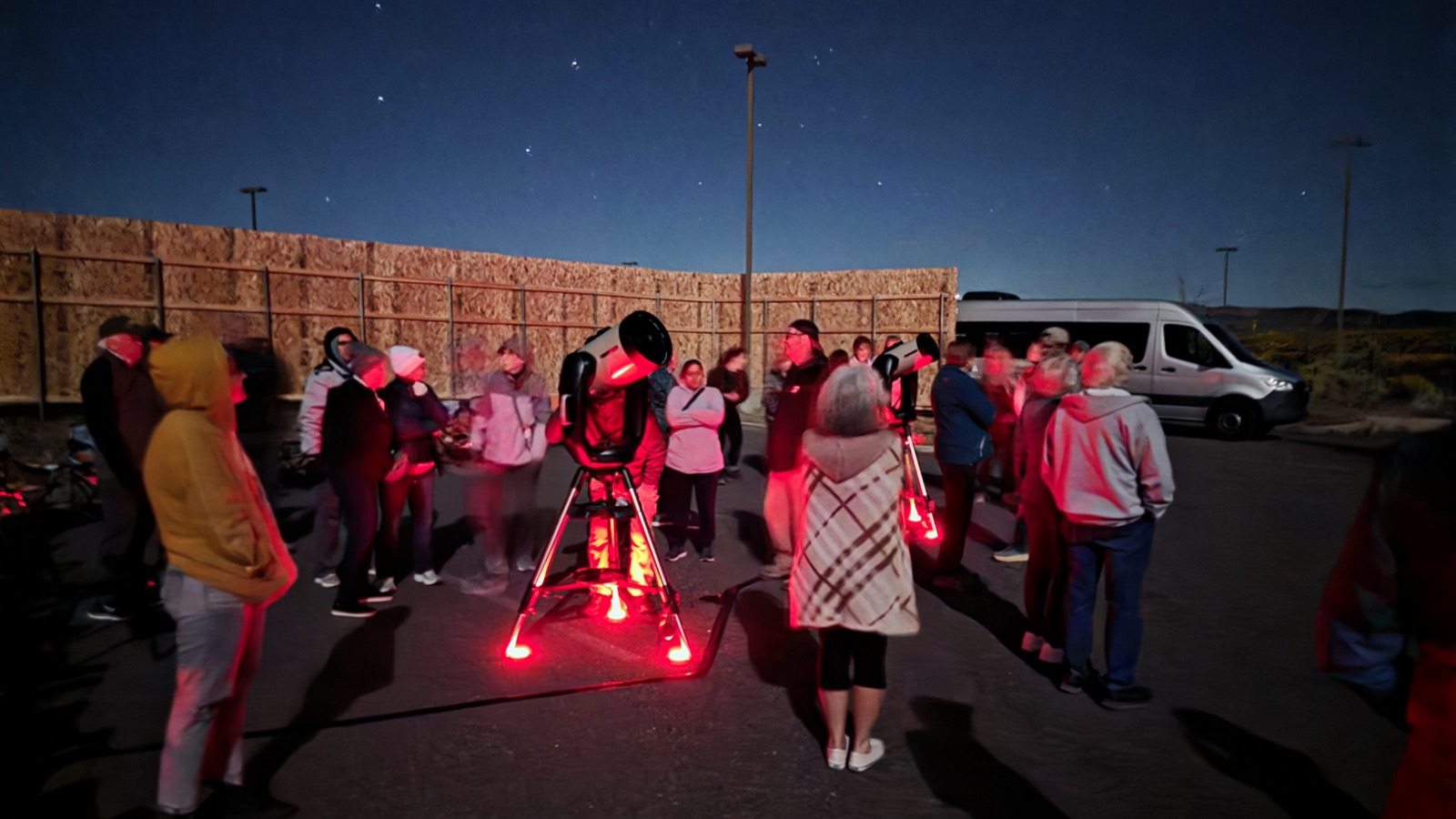 Group of visitors gathered around telescopes and a tour van under the night sky