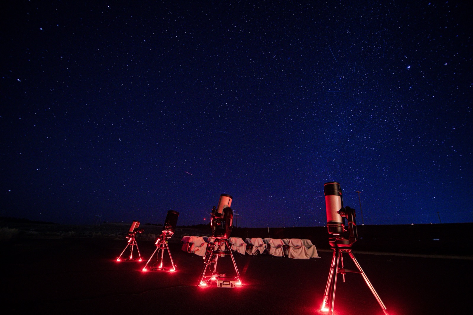 Four telescopes set up under a starry sky, lit by dim red lights to preserve night vision
